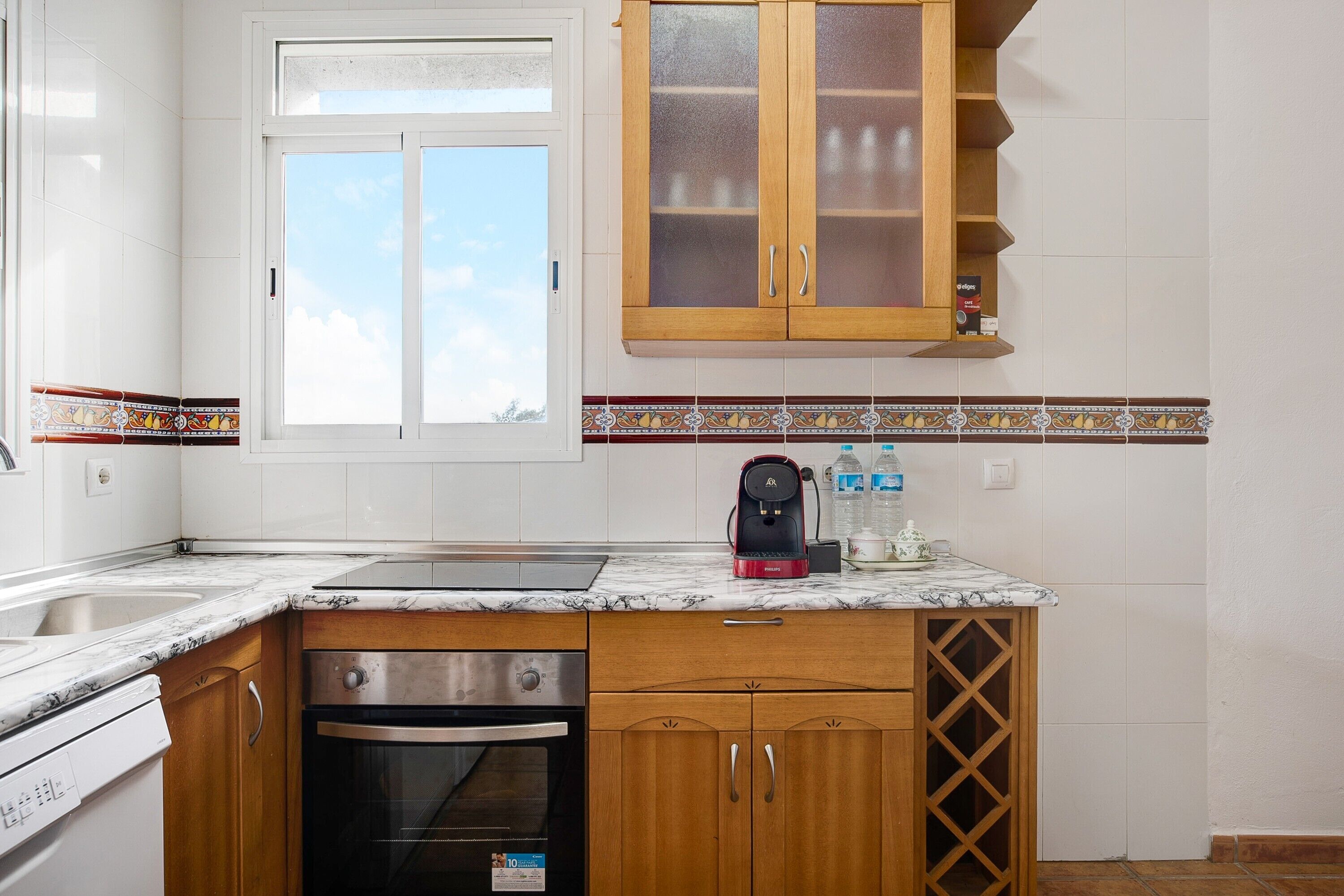 A kitchen with a window, wooden cabinets, a marble countertop, and a coffee maker.