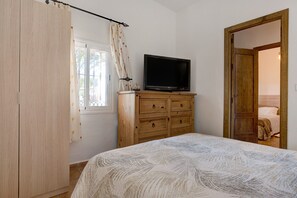 Makuuhuone, jossa on sänky, puinen lipasto, televisio ja ovi, joka johtaa toiseen huoneeseen.