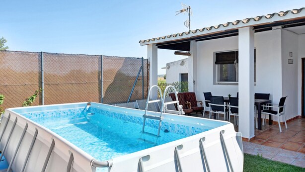 An outdoor swimming pool with a ladder, surrounded by a fenced area, and a patio with outdoor furniture.