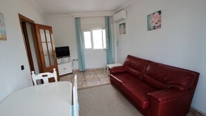 A room with a red leather sofa, a white table, a TV on a cabinet, and a window with curtains. - Apartment 'Celeste' with Sea View, Shared Terrace and Wi-Fi (conil de la frontera)