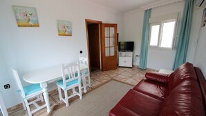 A living room with a red sofa, a white table with chairs, a TV stand, and a door leading to another room. - Apartment 'Celeste' with Sea View, Shared Terrace and Wi-Fi (conil de la frontera)