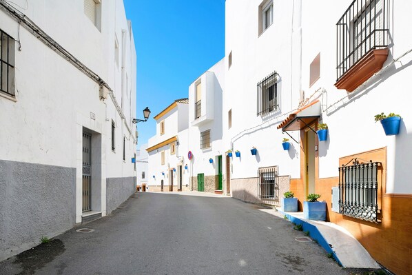 Una calle estrecha bordeada de edificios blancos, algunos con balcones y plantas en macetas.
