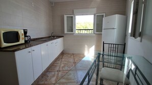 A kitchen with white cabinets, a microwave, a refrigerator, a glass table, and a window with open shutters. - Apartment 'Celeste' with Sea View, Shared Terrace and Wi-Fi (conil de la frontera)