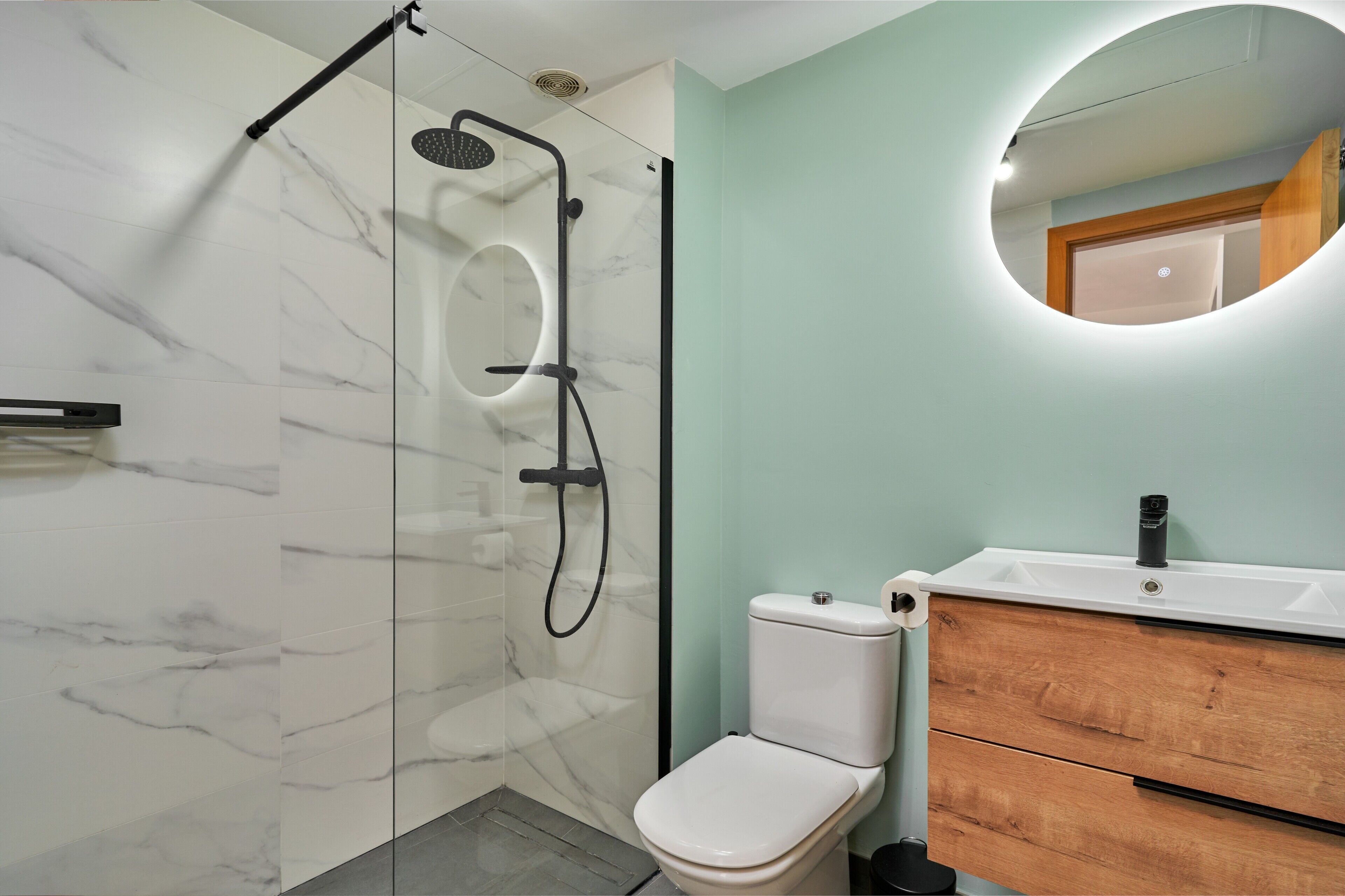 Ein Badezimmer mit Duschkabine, weißer Toilette und einem Holzkosmetikschrank mit Spiegel.