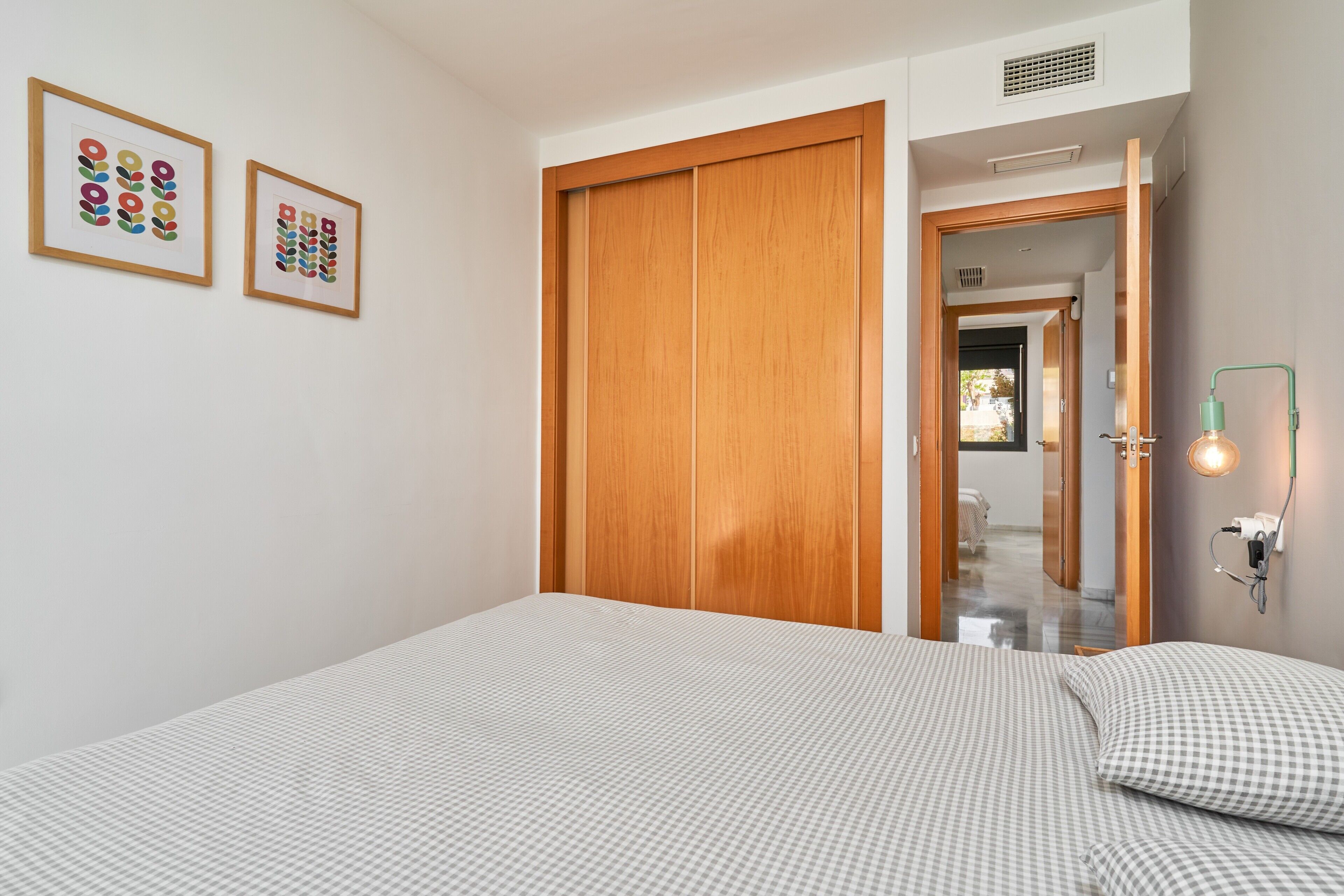 A bedroom with a bed, a wooden wardrobe, and two framed artworks on the wall.