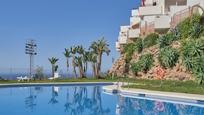 A swimming pool with a clear blue sky, palm trees, and a building with balconies. - '2-Bedroom Apartment with Seaview', Wi-Fi and Air Conditioning (Nerja)