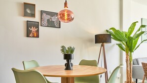 A dining area with a round wooden table, green chairs, a hanging copper pendant light, framed animal pictures on the wall, and a potted plant. - '2-Bedroom Apartment with Seaview', Wi-Fi and Air Conditioning (Nerja)