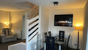 A modern living room with a dining area, a staircase, a cityscape painting, and a radiator. - Rural Chapel Cottage, Near Airport, bar & hot tub (Aberdeen)