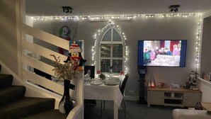 A dining area with a table set for four, a TV mounted on the wall, and a staircase with a railing. - Rural Chapel Cottage, Near Airport, bar & hot tub (Aberdeen)