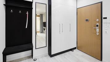 A modern hotel room with a black bench, a large mirror, white wardrobes, and a wooden door with a lock.