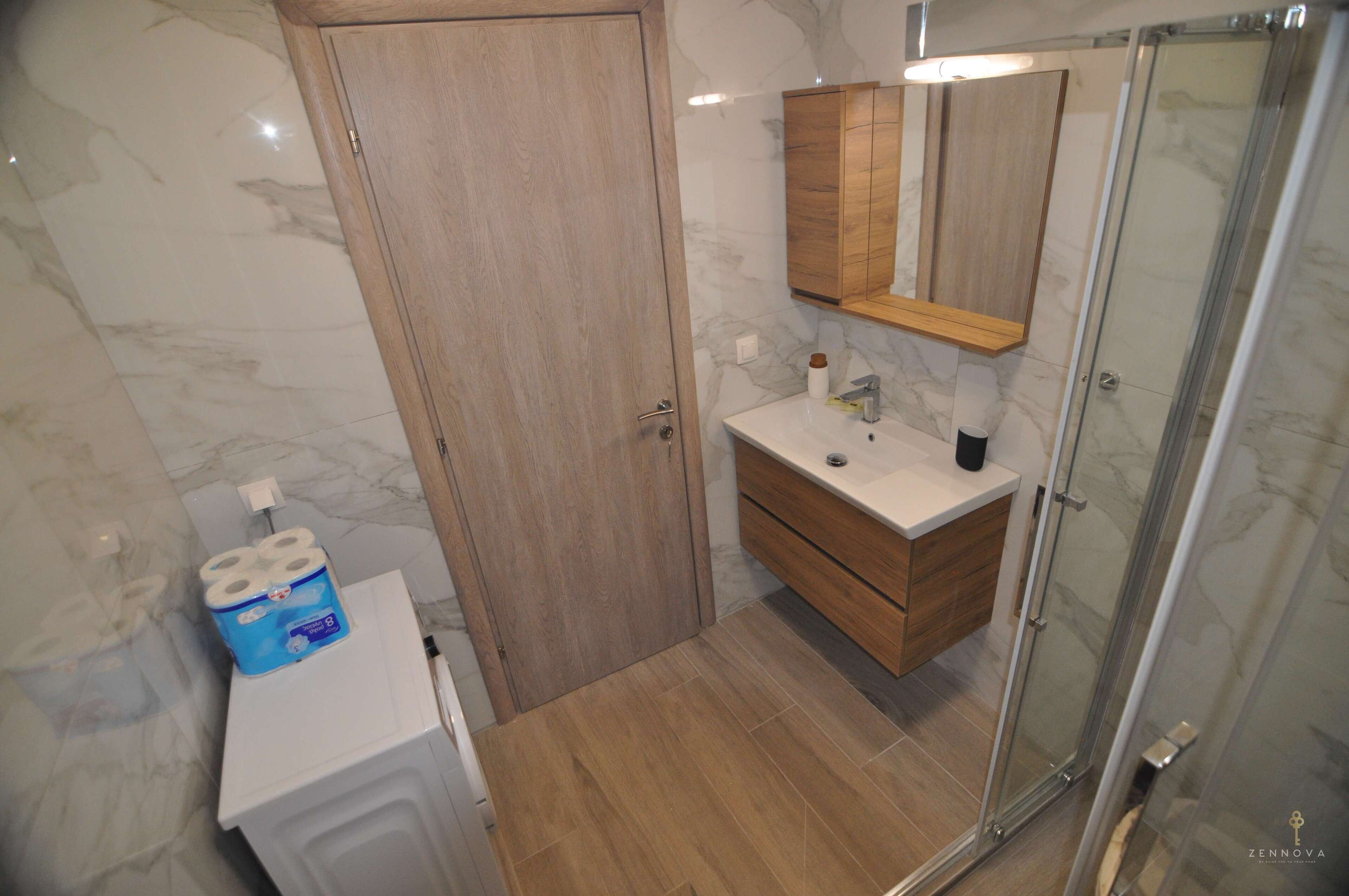 A bathroom with a wooden door, a white sink, a mirror, and a shower area.