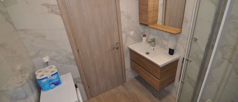 A bathroom with a wooden door, a white sink, a mirror, and a shower area.