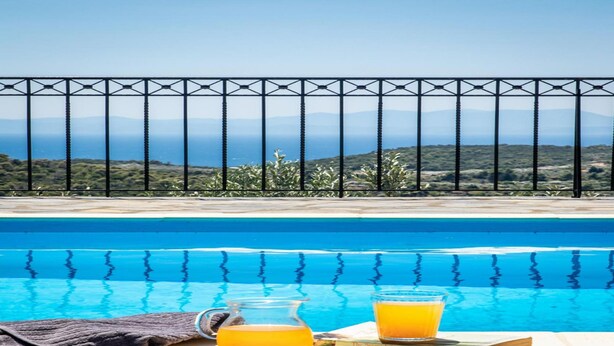 Ein Pool mit freiem Blick auf das Meer und Hügel im Hintergrund.