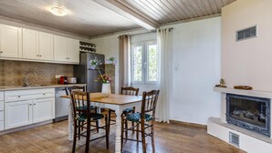 Eine Küche mit weißen Schränken, einem Holzes Esstisch mit vier Stühlen, einem Kühlschrank, einem Toaster und einer Vase mit Blumen.