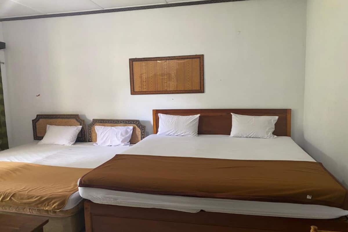 Une chambre d’hôtel avec deux lits, l’un recouvert d’une couverture marron et l’autre de draps blancs.