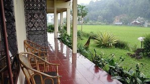 Un espace extérieur abrité, doté de chaises en osier, d’un sol carrelé et offrant une vue sur un champ verdoyant.