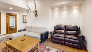 Una sala de estar con sofá, un sillón de cuero, una mesa de centro de madera y un cráneo de ciervo montado en la pared.