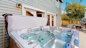 Un jacuzzi frente a una casa con terraza de madera y un hogar a fuego de piedra.