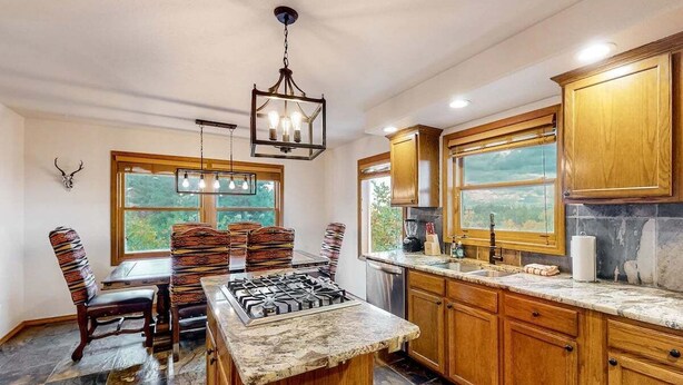 Una cocina con armarios de madera, estufa a gas, lámpara de araña y ventanas amplias.