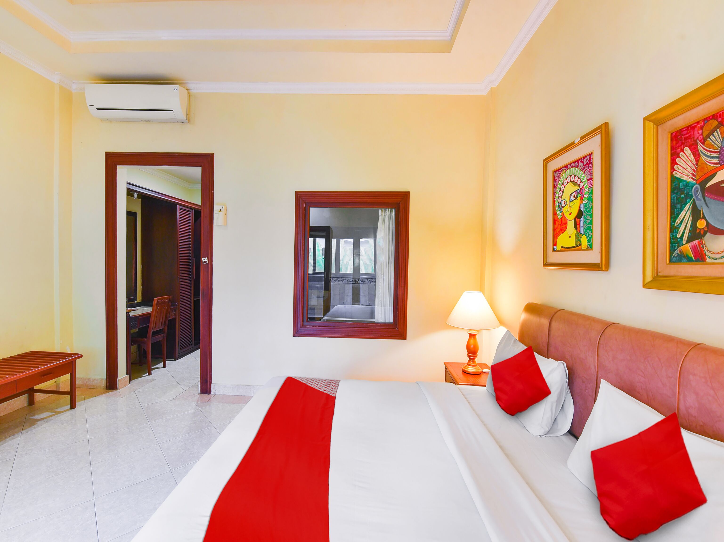 A hotel room with a bed, a desk, a chair, a lamp, and artwork on the walls.