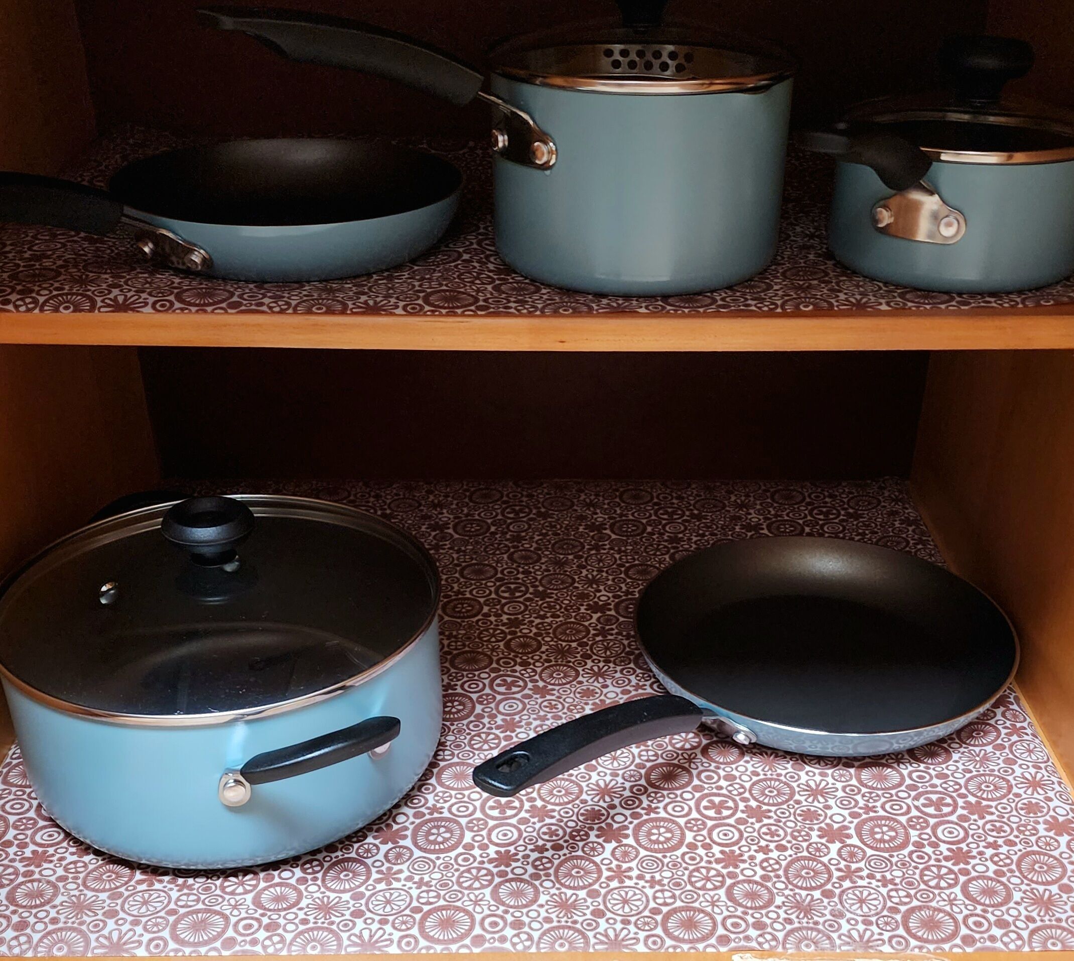 Eine Küche mit einem gemusterten Boden, einem blauen Topf mit Deckel, einer Bratpfanne und einem kleineren Topf auf dem Regal.