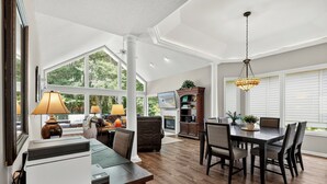 A spacious living area with a dining table, chairs, a fireplace, and a large window offering a view of greenery.