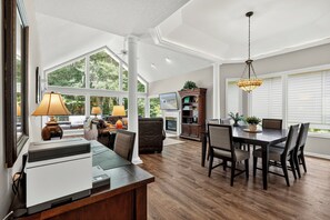 A spacious living area with a dining table, chairs, a fireplace, and a large window offering a view of greenery.