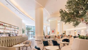 Un moderno vestíbulo de hotel con un área de estar central, un bar con estantes de productos y grandes ventanales.
