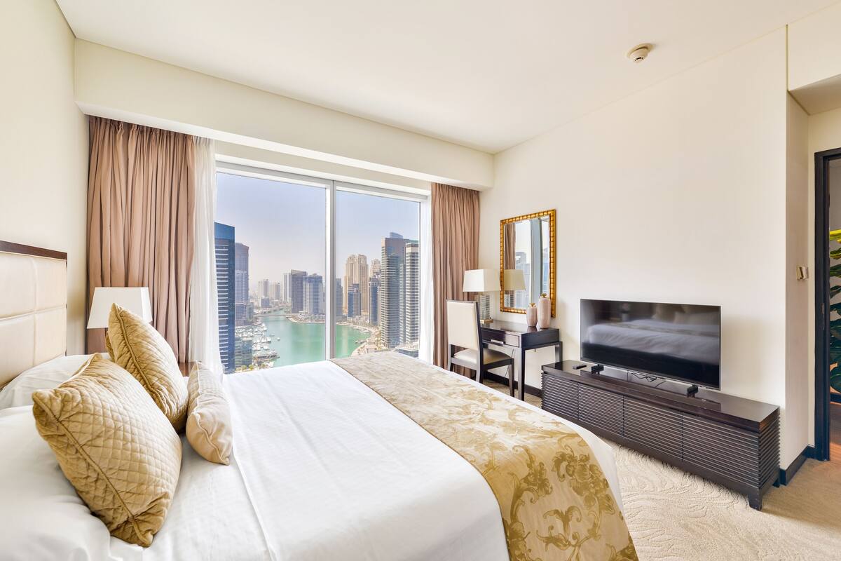 A hotel room with a large bed, a desk with a TV, and a view of a cityscape.