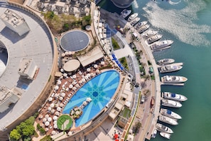 An aerial view of a waterfront hotel with a pool, sun loungers, and boats docked at the pier. - Address Dubai Marina Residences (Dubai)