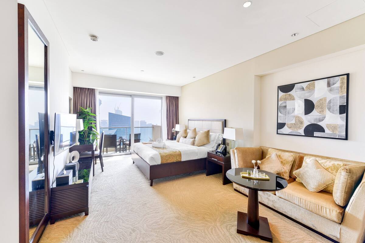 A hotel room with a large bed, a sofa, a small table, and a view of the city.