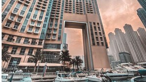 Un edificio alto con un gran arco de entrada, rodeado de agua y barcos, con otro edificio y un avión al fondo.