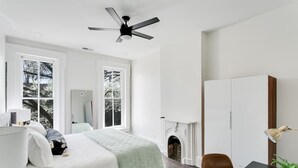 Un dormitorio moderno con una cama grande, una chimenea, un escritorio y un ventilador de techo.