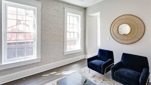 Una habitación amplia con ventanas grandes, un espejo moderno y dos sillones oscuros.