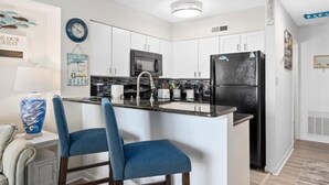 A modern kitchen with white cabinets, a black refrigerator, and a blue island with two bar stools.