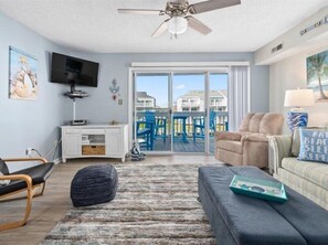 A spacious living room with a large window, a ceiling fan, a flat-screen TV, and a comfortable seating area.