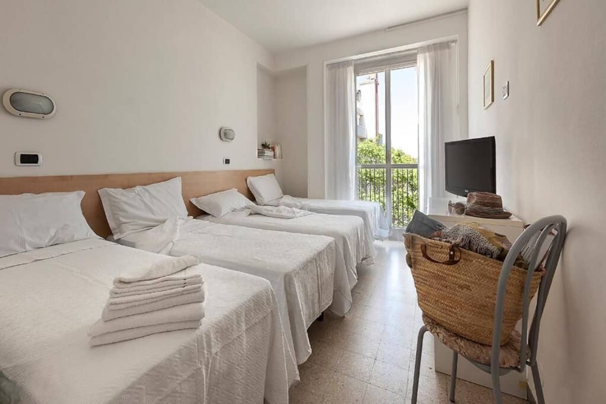 A hotel room with three beds, a TV, a balcony, and a wicker chair.