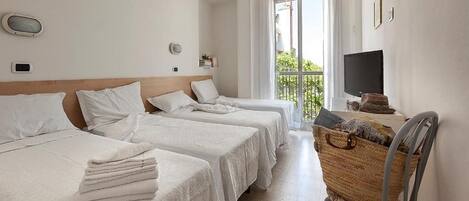A hotel room with three beds, a TV, a balcony, and a wicker chair.