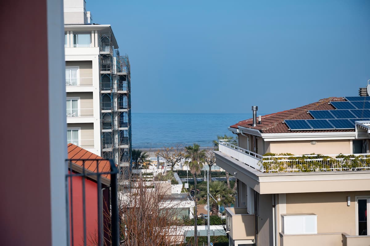 A high-rise building with a view of the sea, solar panels on the roof, and a balcony with plants.