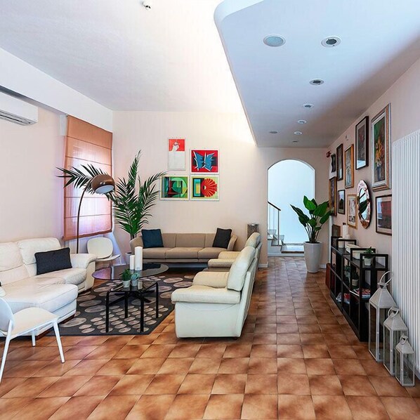 Un salon spacieux avec un ensemble de canapés, une table basse et une plante en pot. Des tableaux encadrés ornent le mur et un radiateur se trouve à droite.