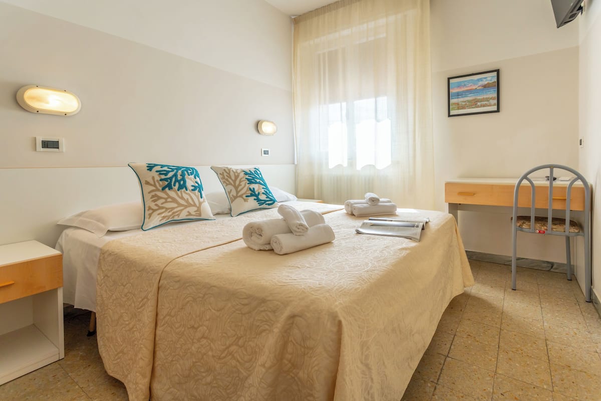 A hotel room with a bed, a desk, a chair, and a window with curtains.
