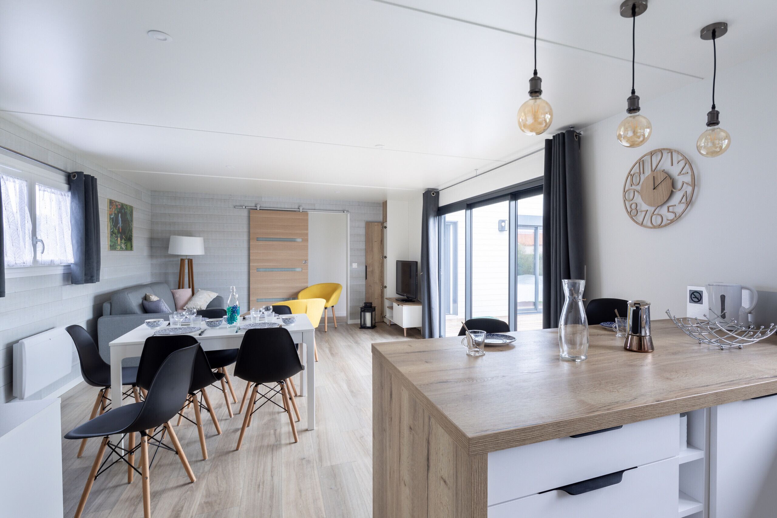 Une cuisine moderne avec un îlot central en bois, un coin repas avec des chaises et une grande fenêtre.