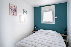 A bedroom with a white bed, teal walls, a window, and two framed pictures on the wall.