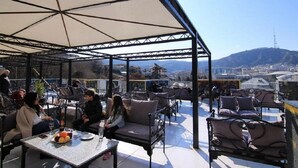 Un espace extérieur aménagé avec des tables et des chaises, offrant une vue sur le paysage urbain et les montagnes en arrière-plan.