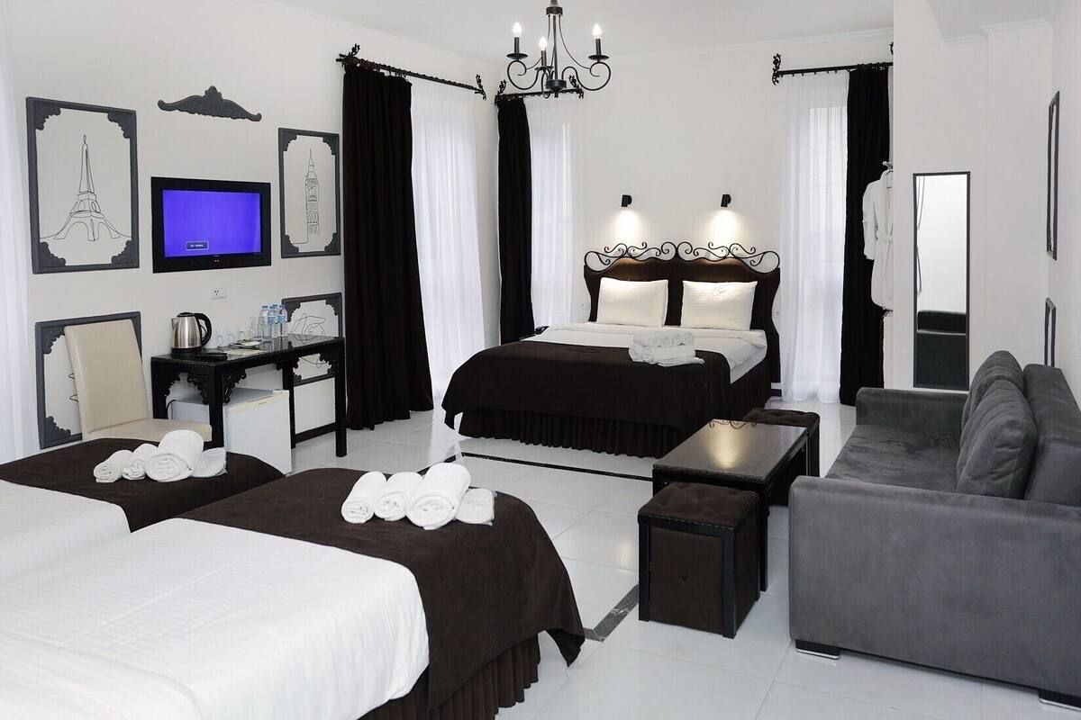 A hotel room with a large bed, two smaller beds, a sofa, a desk with a computer, and a chandelier.
