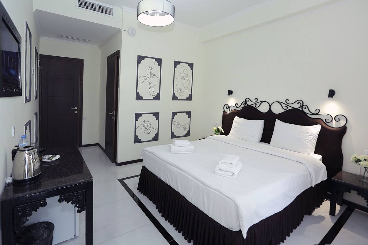 A hotel room with a large bed, a bedside table with a lamp, and a small table with a vase of flowers.