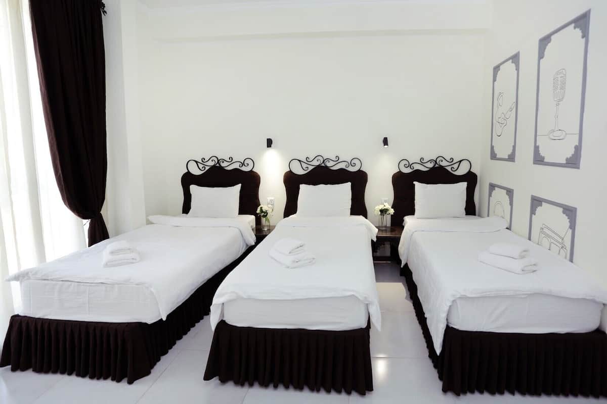 A hotel room with two single beds, dark headboards, white bedding, and a small table with a vase of flowers.