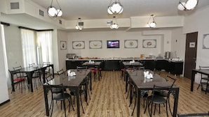 Un espace repas avec plusieurs tables et chaises, un comptoir central où sont présentés les plats, et des luminaires au plafond.