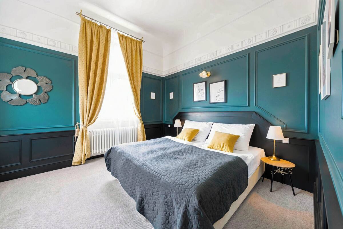 A bedroom with a large bed, a bedside table with a lamp, and a window with curtains.