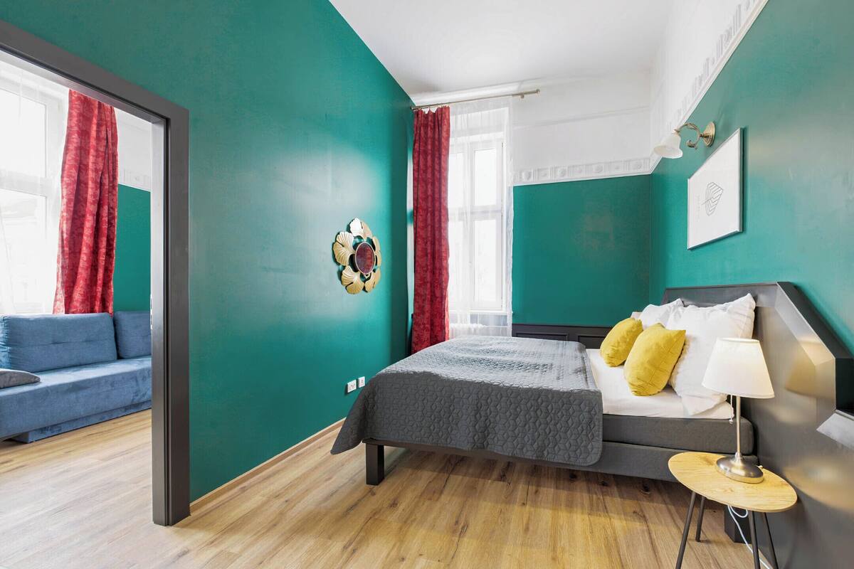 A bedroom with a bed, bedside table, and a view of a balcony.